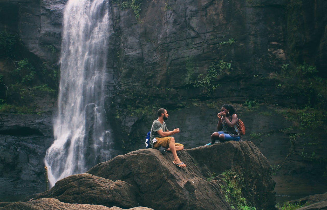 Two friends resting on rocks beside a waterfall, taking in an awe-inspiring view