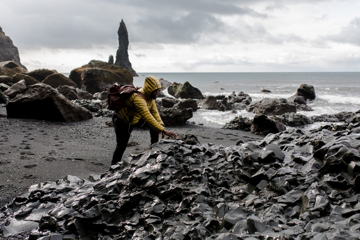 Backpacker in a rain jacket scrambling over rugged volcanic rock on a remote trail